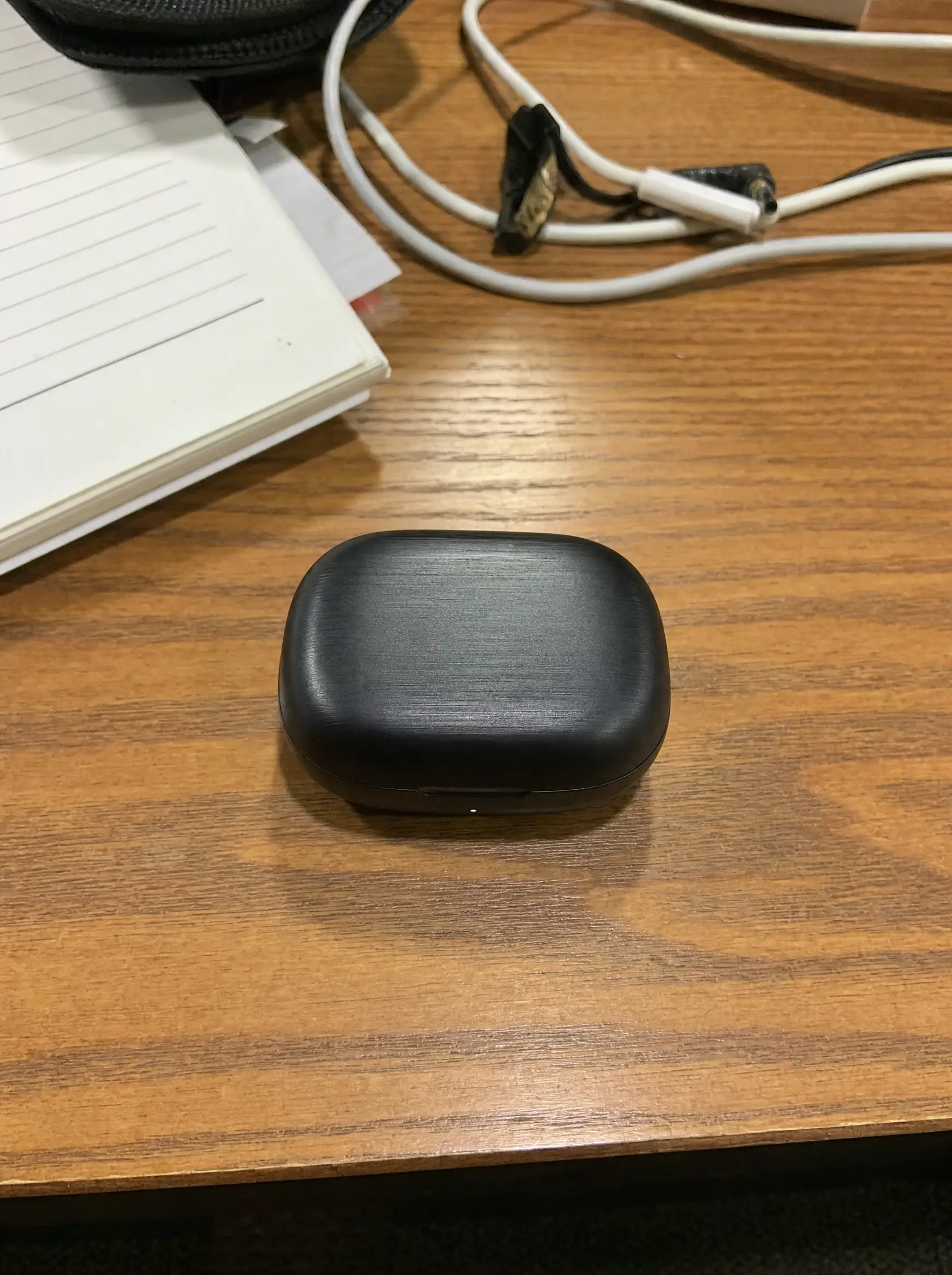 An earbuds case photographed at home on a cluttered desk